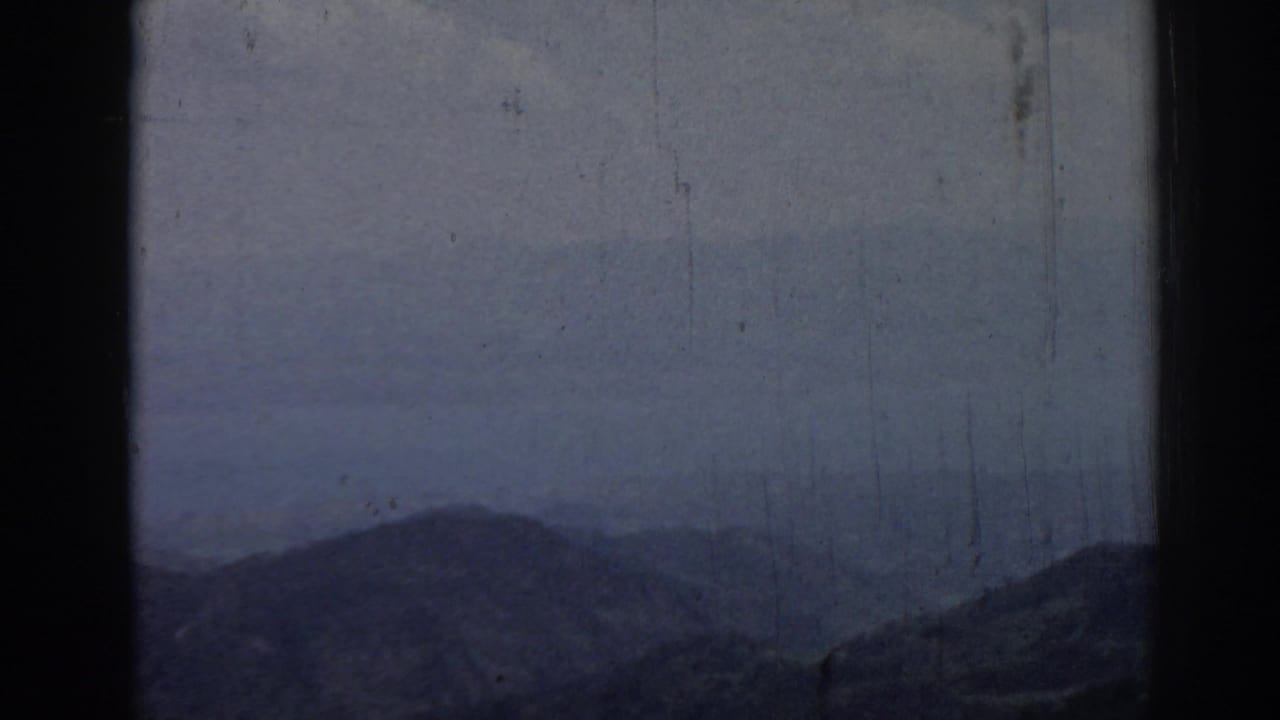 Hazy 1962 Ephesus mountain view with layered ridges, muted sky, visible scratches, and dark 8mm frame edges.