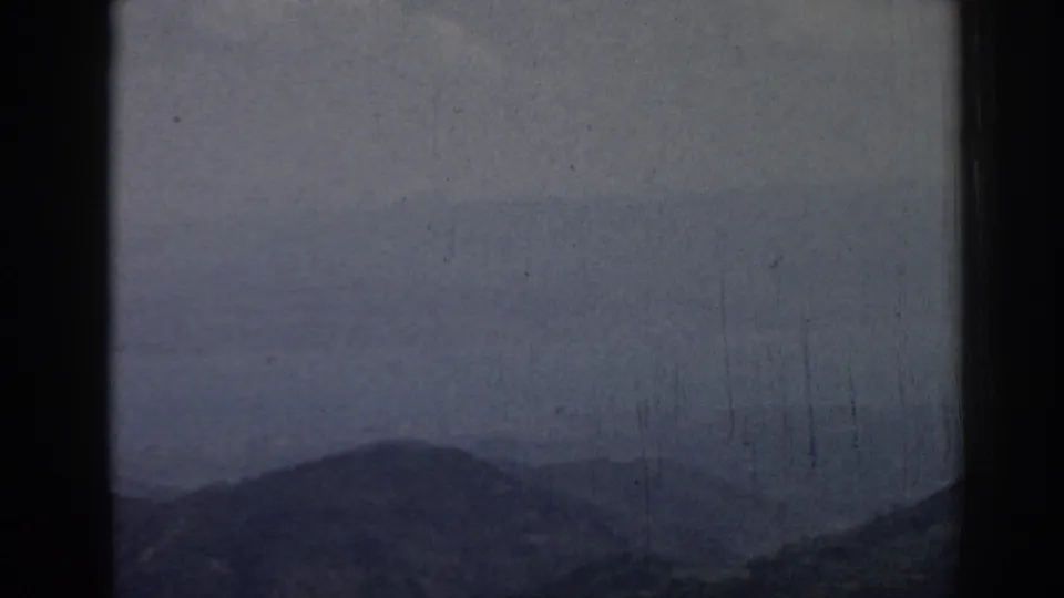 1962 8mm frame from Ephesus showing blue-gray hills, distant haze, pale sky, and visible film wear.