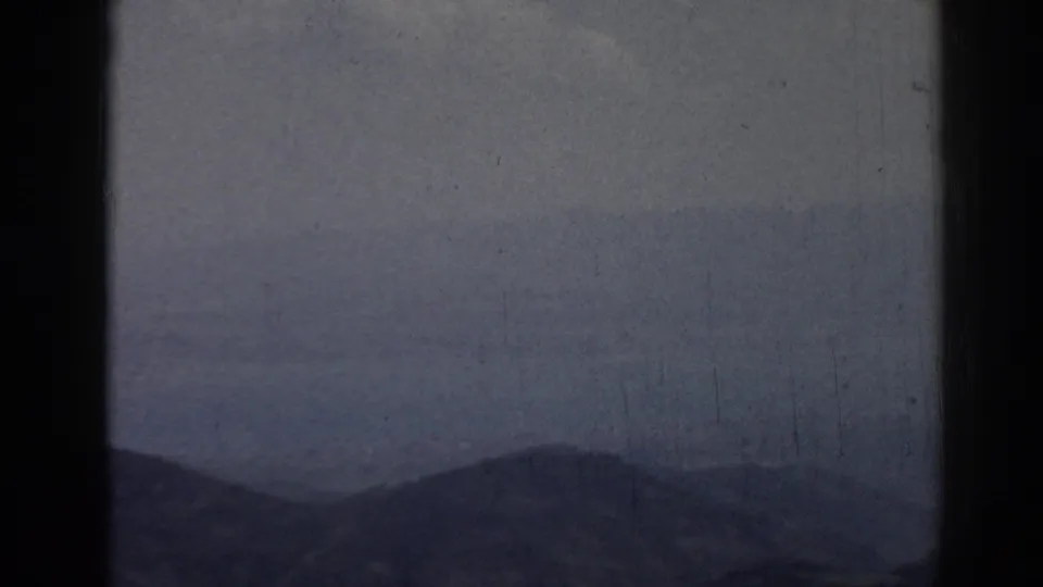 Hazy 1962 Ephesus landscape frame with a low mountain ridge, soft sky, dust, scratches, and dark film gate edges.