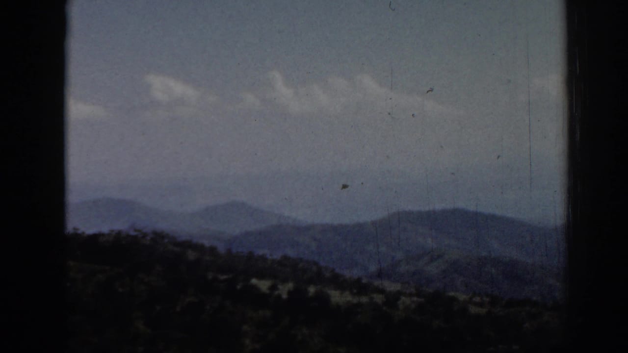 Layered mountain ridges beneath a hazy sky with dark film borders.