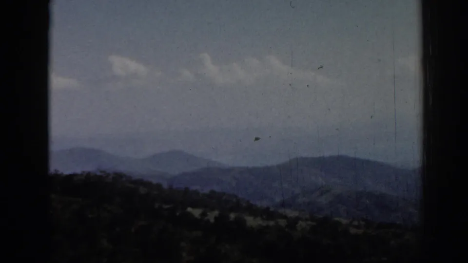 1962 8mm travel frame from Ephesus, Turkey, showing distant mountain ridges, wooded foreground, pale clouds, and dark gate borders.