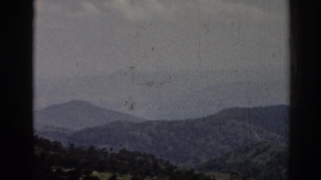 Late-frame 1962 Ephesus landscape view with overlapping hills, muted sky, dark 8mm borders, and visible scratches and specks.
