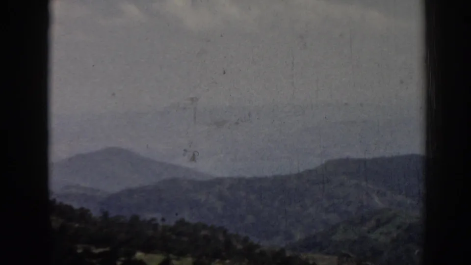 Late-frame 1962 Ephesus landscape view with overlapping hills, muted sky, dark 8mm borders, and visible scratches and specks.