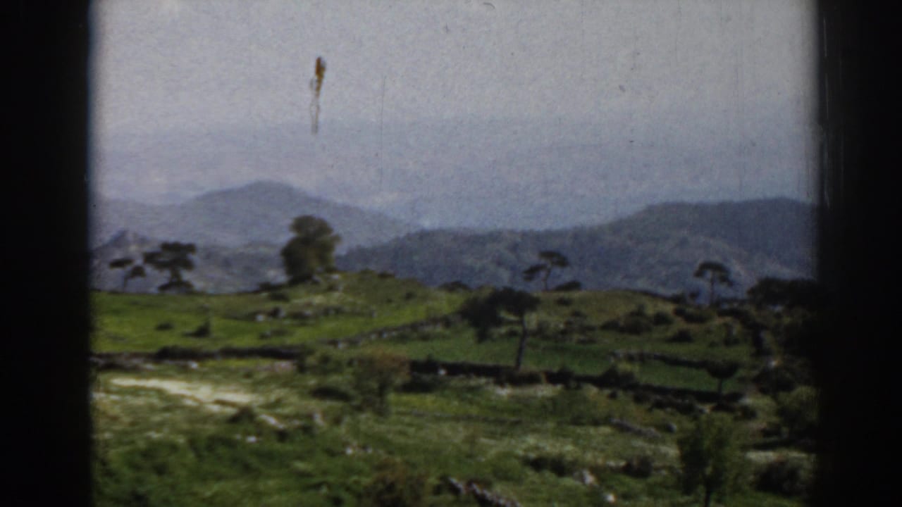 1962 8mm view near Ephesus showing green hills, low walls, scattered trees, and blue-gray mountains beyond.