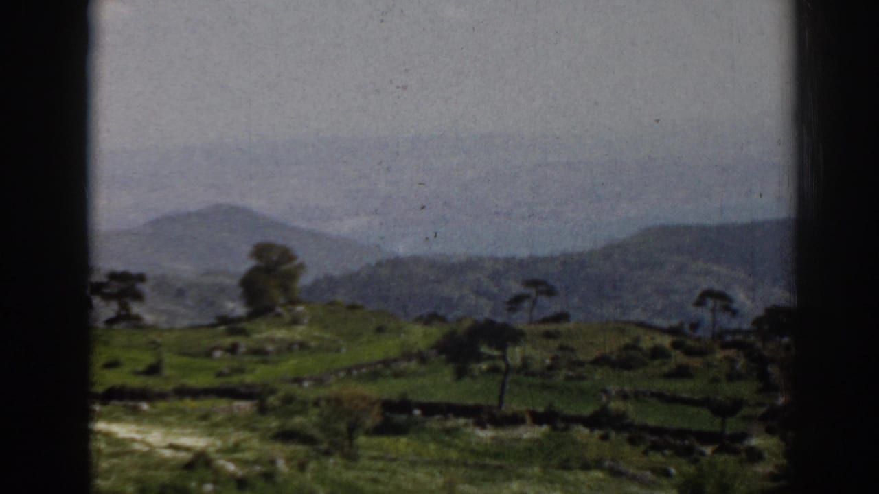 Moving 8mm view near Ephesus, Turkey, with rural green fields, scattered trees, stone walls, and misty hills.