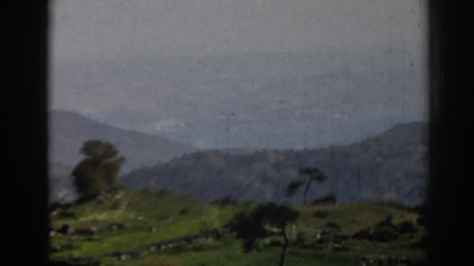 1962 home-movie frame near Ephesus showing a closer hillside view with trees, walls, and soft mountain background.