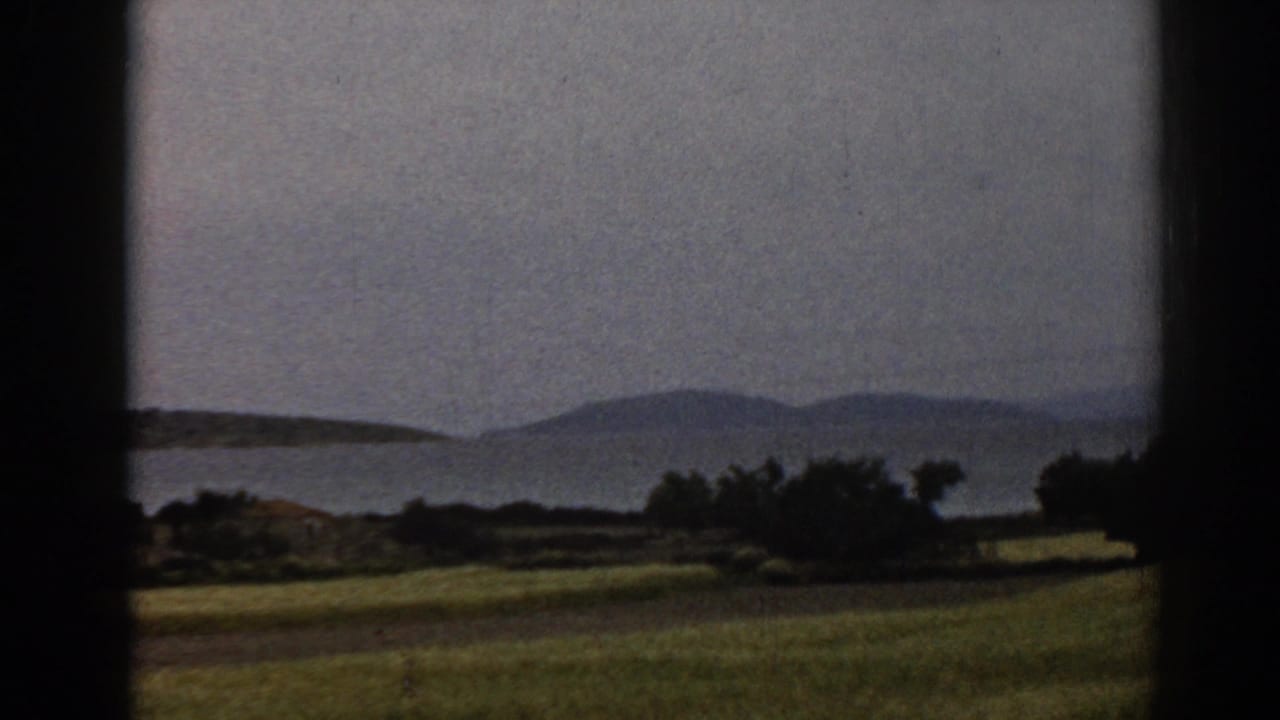 1962 8mm view near Ephesus, Turkey, with fields, shrubs, water, and distant hills passing behind dark frame or window edges.