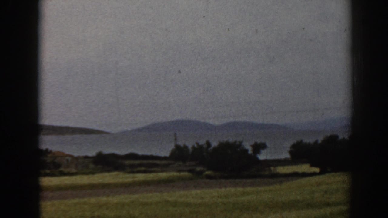 1962 8mm rural landscape near Ephesus, Turkey, showing an open field, shoreline shrubs, water, and hazy hills from a moving vehicle.