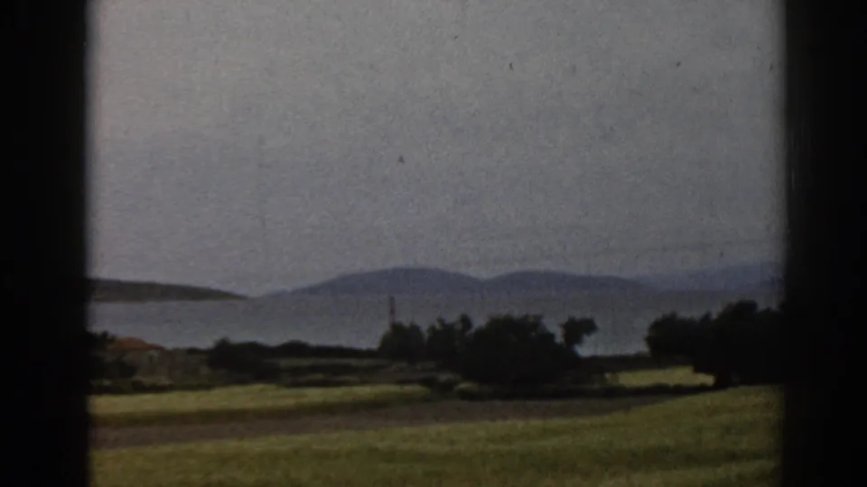 1962 8mm rural landscape near Ephesus, Turkey, showing an open field, shoreline shrubs, water, and hazy hills from a moving vehicle.