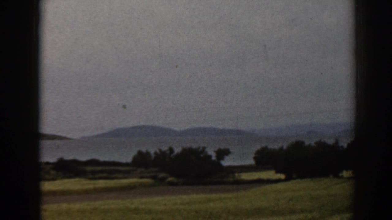 Green fields and trees with distant hills, seen through dark vertical frame edges.