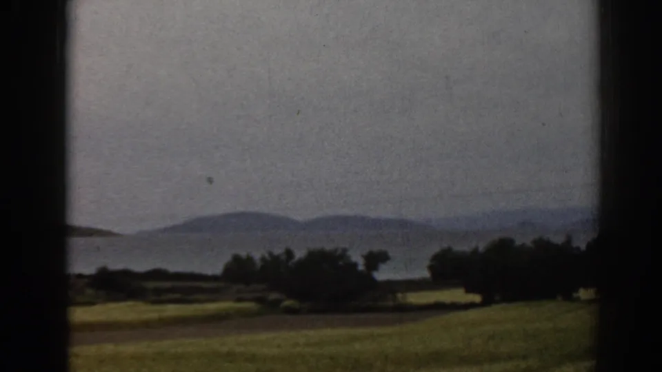 1962 Ephesus-area landscape with fields, trees and hazy distant hills framed by dark edges on 8mm film.