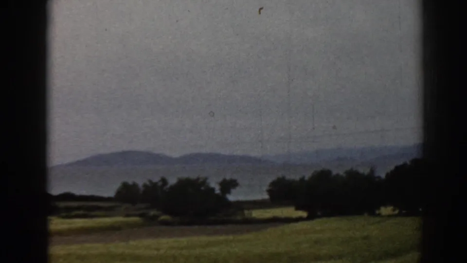 8mm home-movie frame of the Ephesus-area countryside, with trees, fields and distant mountains under haze.