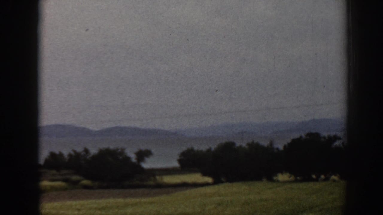 1962 8mm view of rural Ephesus-area terrain with soft fields, trees and low mountains beyond.
