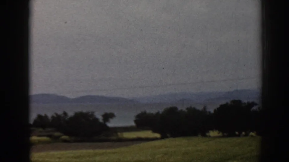 1962 8mm view of rural Ephesus-area terrain with soft fields, trees and low mountains beyond.