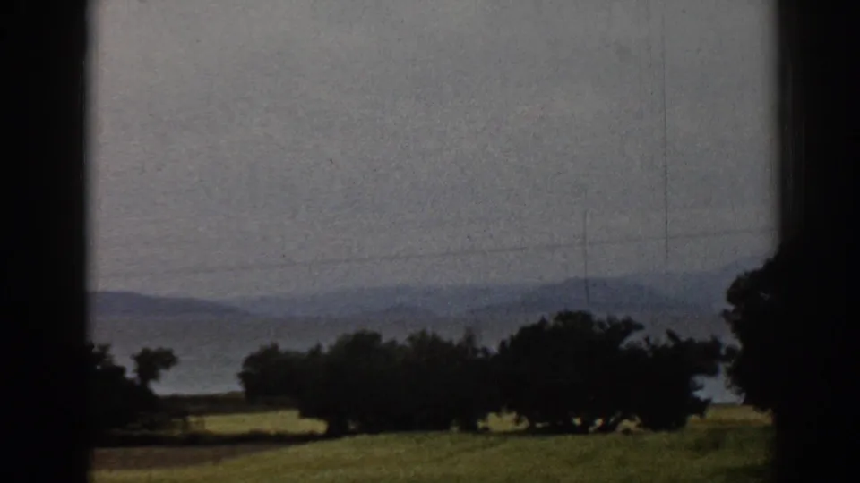 1962 Ephesus countryside view with grass, silhouetted trees, distant hills, power lines, and dark framing from a window or opening.