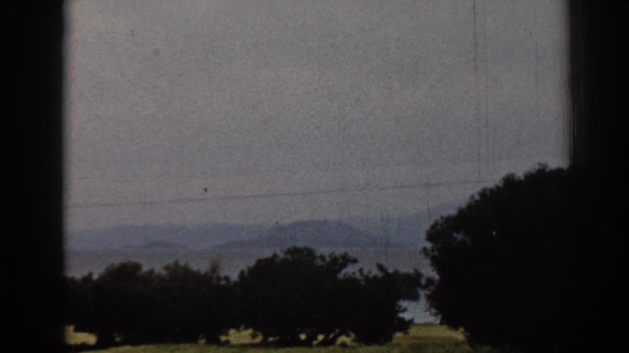Late frame of the 1962 Ephesus countryside view, showing dark trees, hazy hills, power lines, and shadowed film-frame borders.