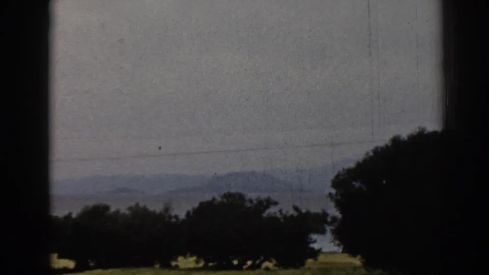 Late frame of the 1962 Ephesus countryside view, showing dark trees, hazy hills, power lines, and shadowed film-frame borders.