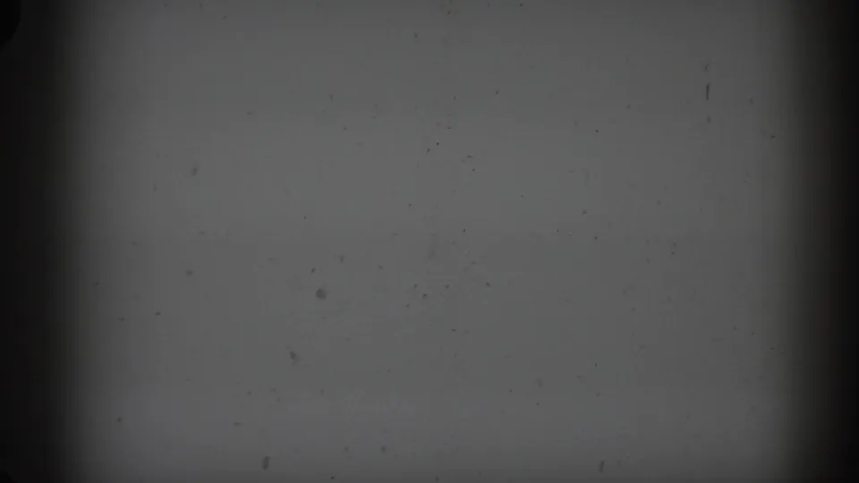 Damaged opening 8mm frame with a blank gray field, dust specks, and a dark vertical film edge before the rural car scene appears.