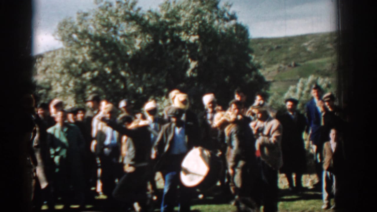 A crowd of men stands in a field, with one person bending near a large drum.