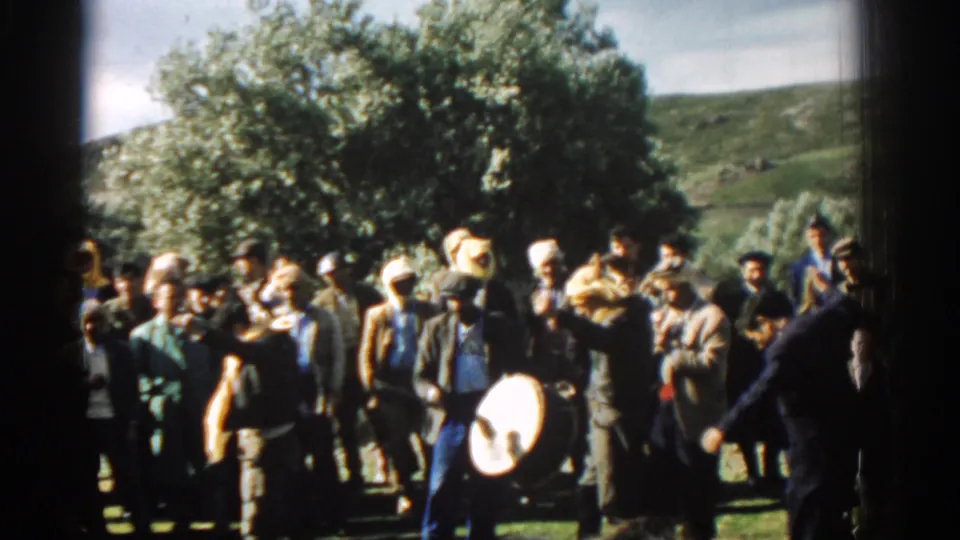 1962 Izmir home-movie frame showing men clapping and watching a drummer during an outdoor gathering.