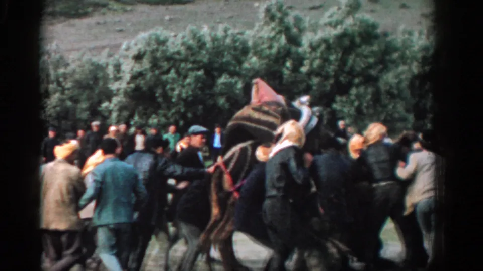 In supplied 1962 Izmir footage, a crowd surrounds a loaded camel while several adults appear to guide or steady it outdoors.
