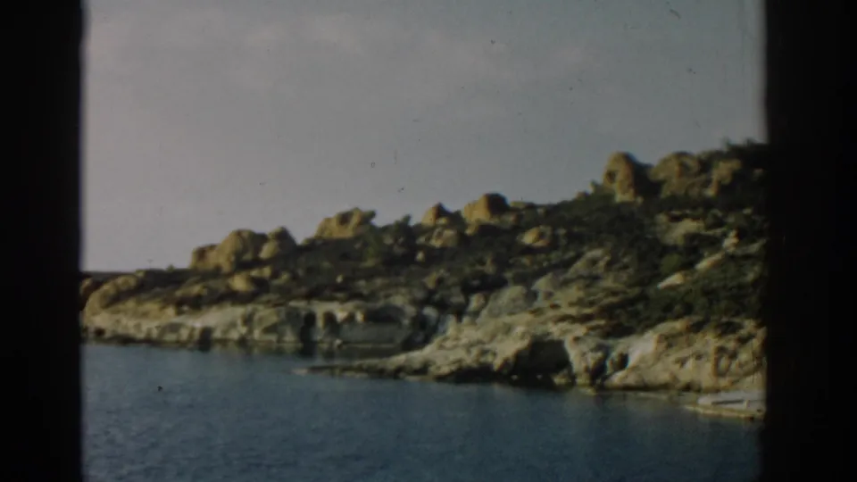 1962 Izmir home-movie view of a rocky shoreline, calm blue water, pale sky, and dark vertical frame borders from the film scan.