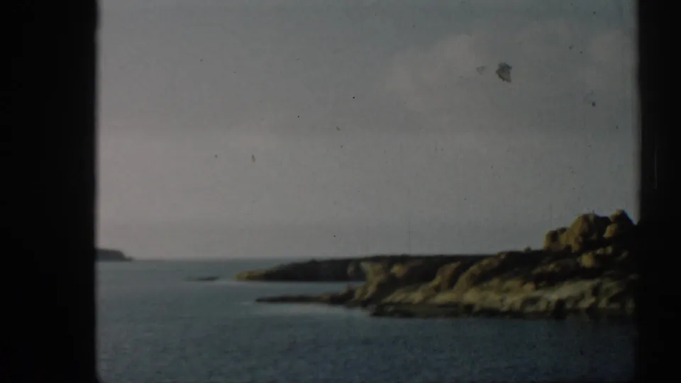 1962 Izmir coastal frame showing open water between low rocky landforms, with muted color and visible 8mm film wear.