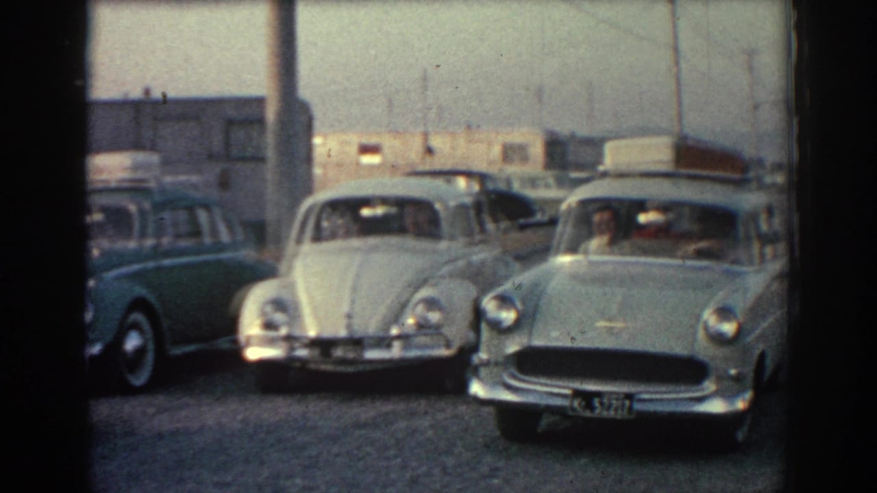 A white Beetle and a light green car pull into a gravel lot.