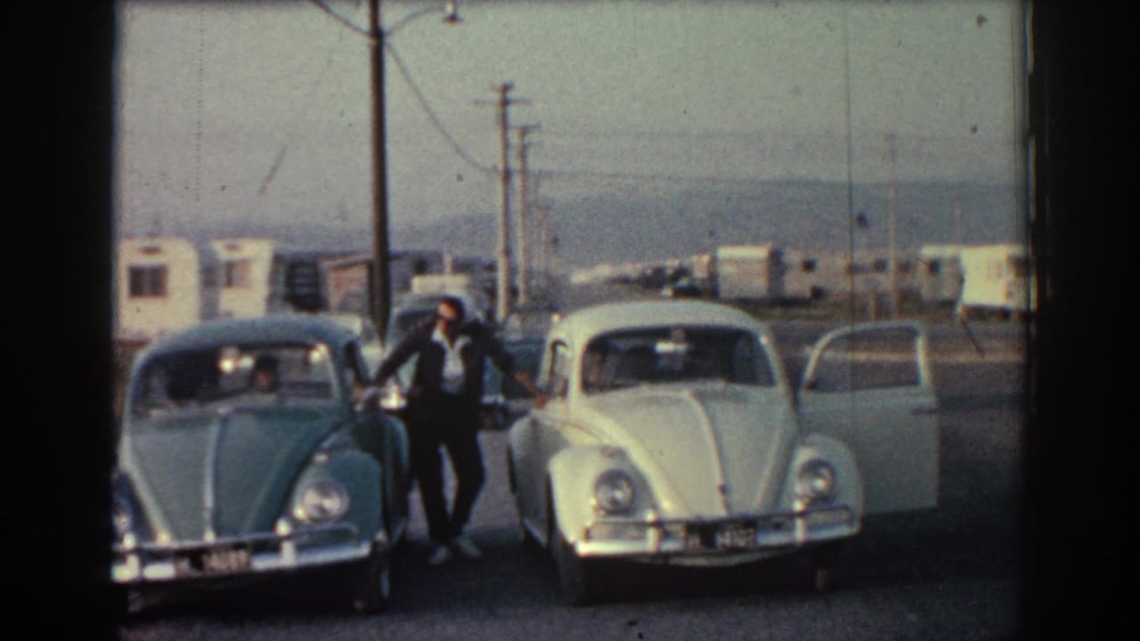 Man standing between two parked rounded cars at a roadside stop.