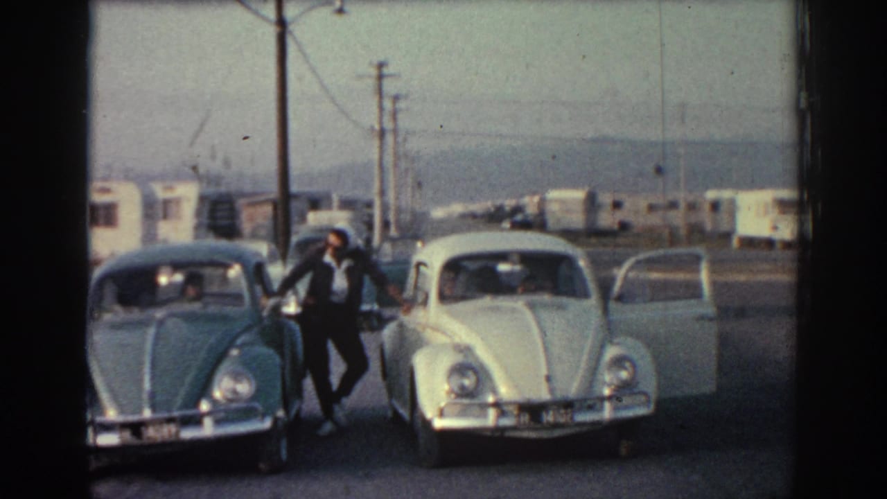 Man leaning near two parked cars with one door open beside a roadside.