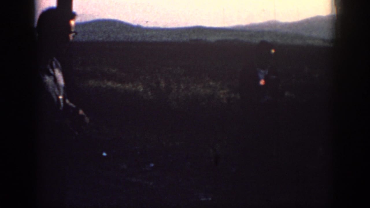 In Rhodes, Greece, 1962, two adult men appear silhouetted in a field at sunset, with distant hills on the horizon.