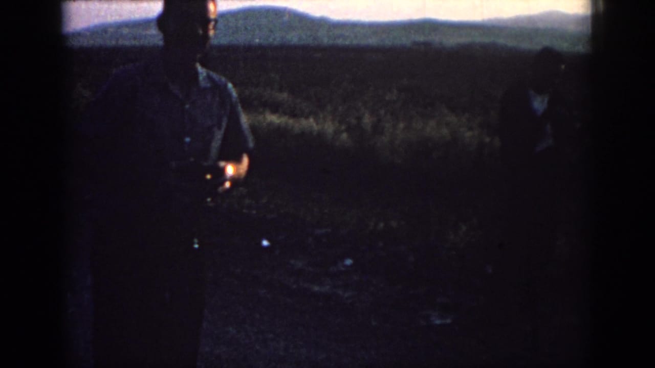 A man stands near the center of a dark field while another figure is partly visible at the edge.