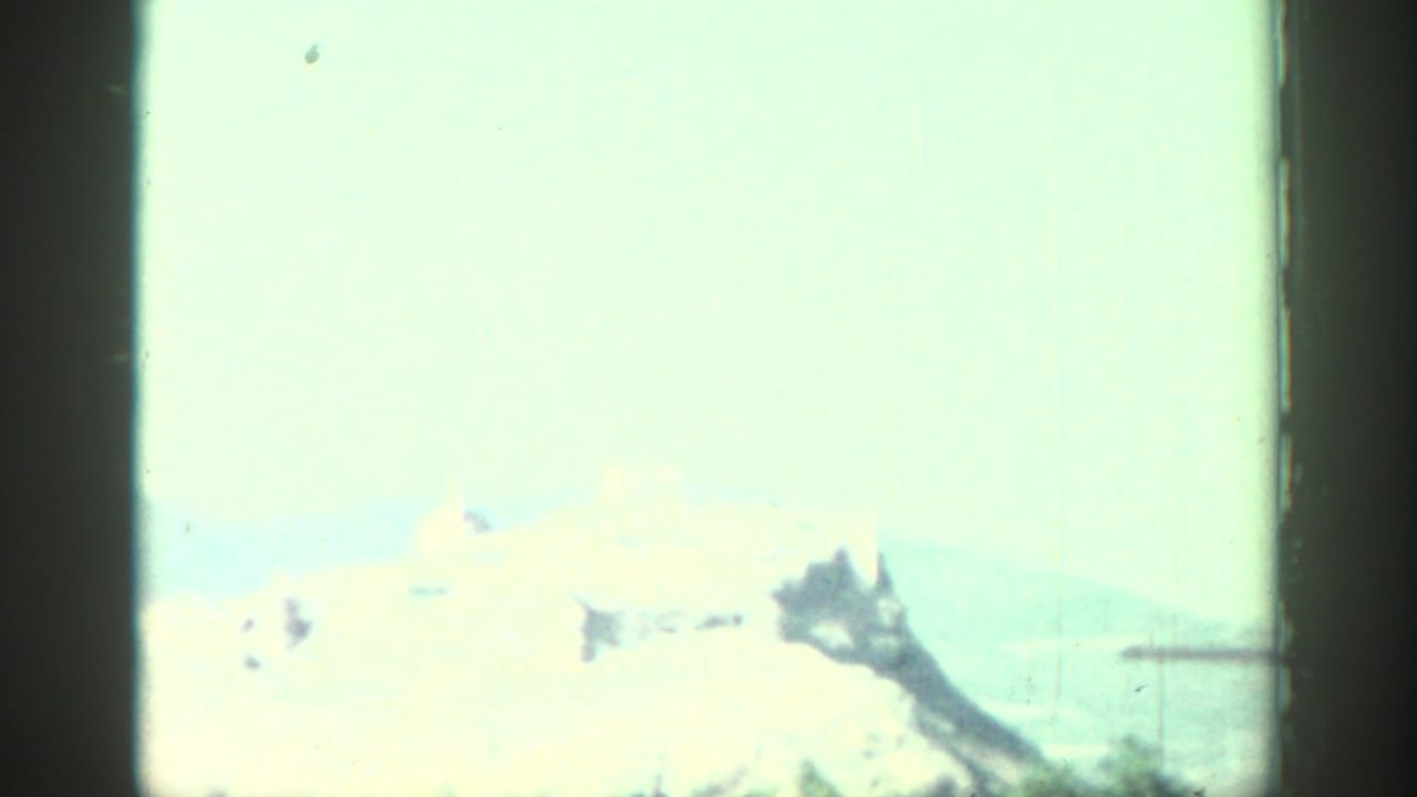 Overexposed distant hilltop ruins seen through an 8mm film frame.