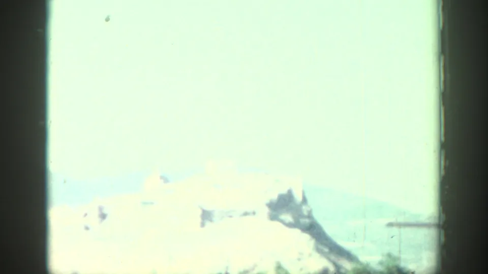1962 Rhodes home-movie frame with a bright, washed-out view of distant hilltop ruins under a pale sky.