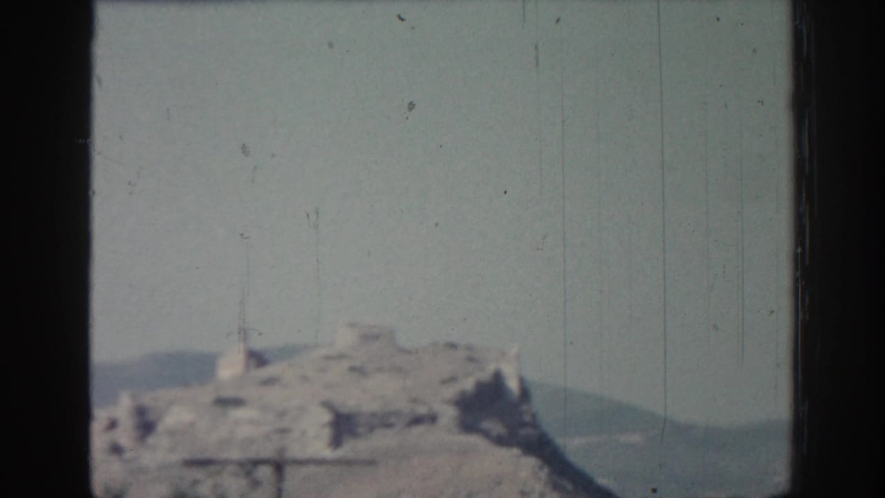 1962 Rhodes footage shows a distant rocky hilltop ruin with a low ridge behind it and visible film scratches.