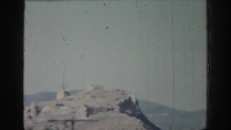 1962 Rhodes footage shows a distant rocky hilltop ruin with a low ridge behind it and visible film scratches.