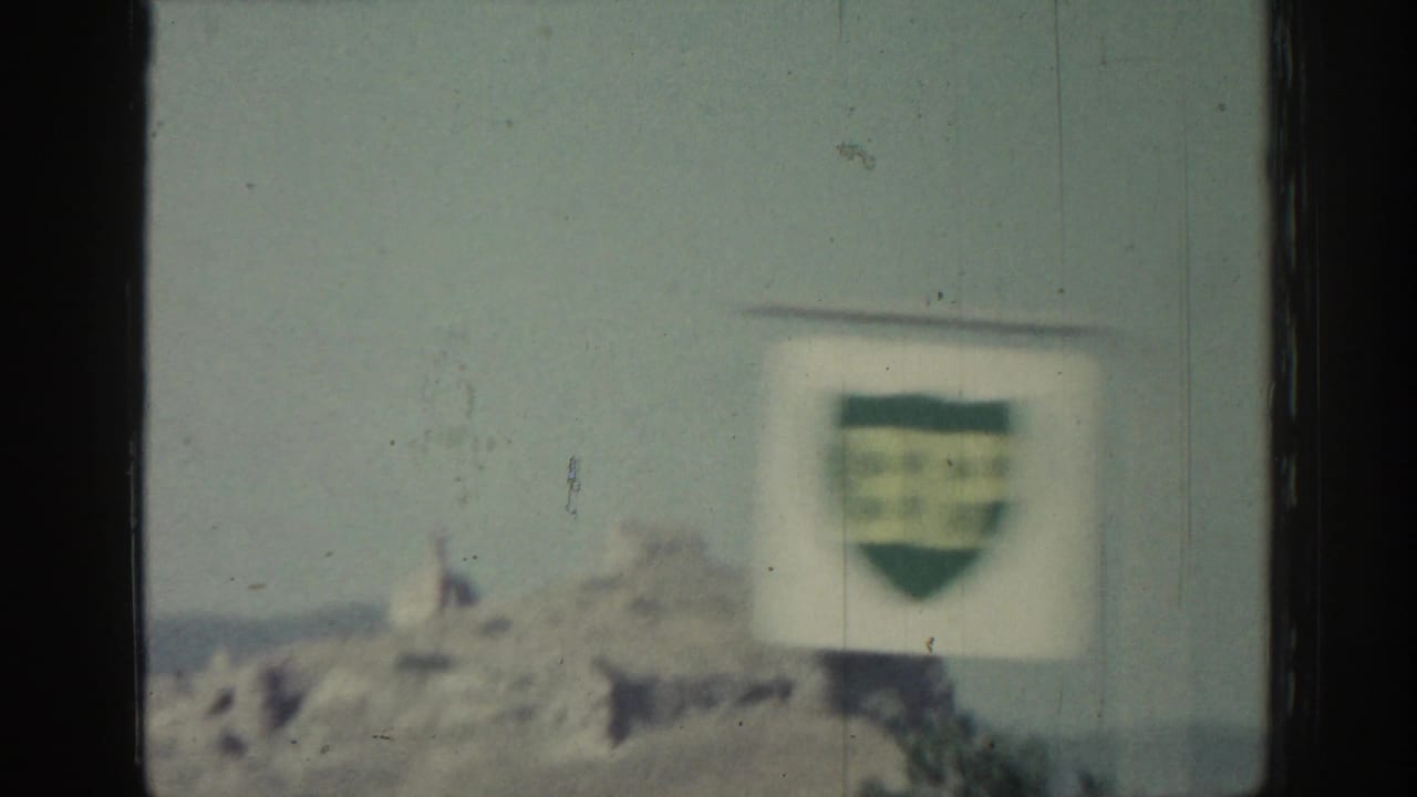 Blurred roadside sign and distant ruins or hilltop forms seen from a moving vehicle.