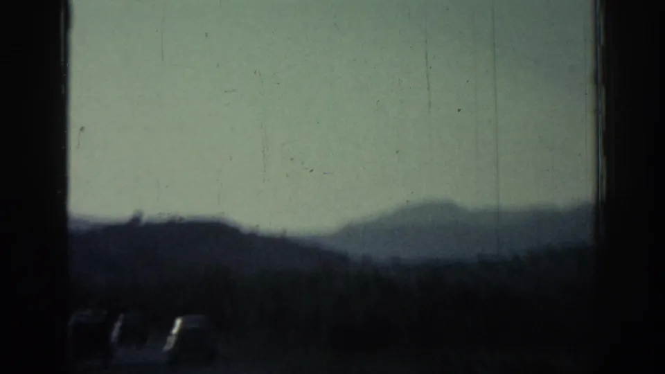 Soft 8mm view from Rhodes, Greece, showing cars near the roadside with a hazy mountain slope beyond.