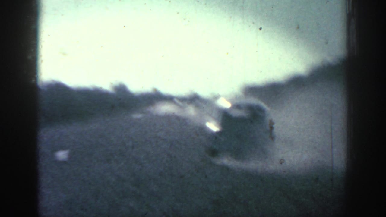 Blurred car ahead on a dusty gravel road seen through a film-frame edge.