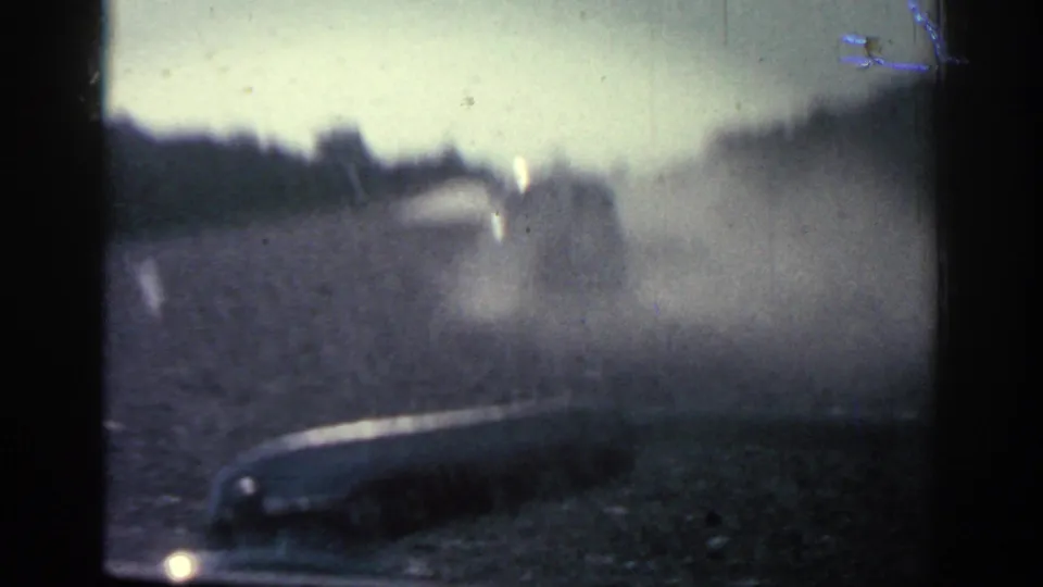 1962 Rhodes home-movie frame showing a dusty road through a windshield or open vehicle view, with a vehicle ahead and trees along the road.