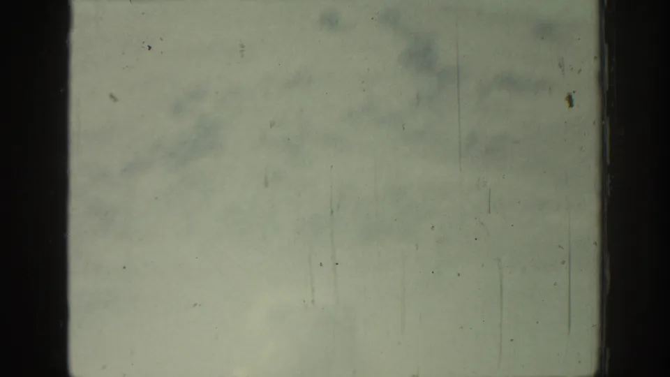 Damaged 8mm home-movie frame with greenish fading, surface marks, and only faint traces of the original outdoor scene.