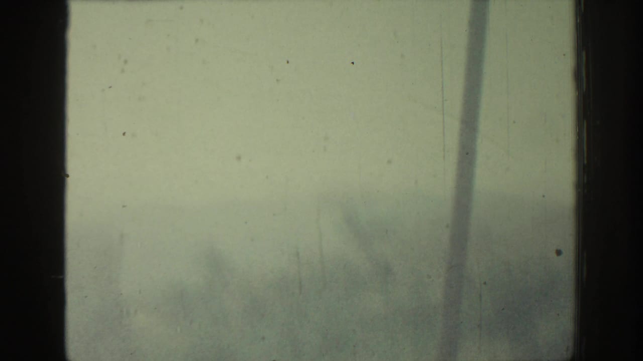 Soft, overexposed landscape behind a central dark window post and visible film scratches.