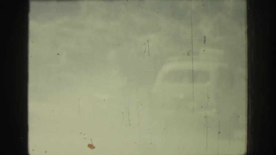 1962 Rhodes 8mm frame showing a washed-out vehicle view with dark window edges, faint arid scenery, dust, and scratches.