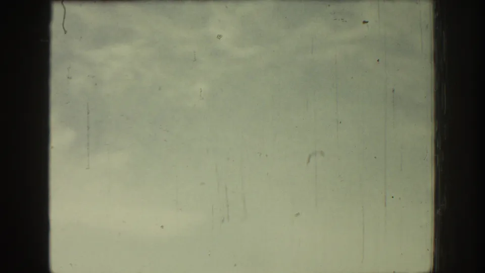 Late frame from 1962 Rhodes home-movie travel footage, showing a hazy roadside view through vehicle-window framing on scratched 8mm film.