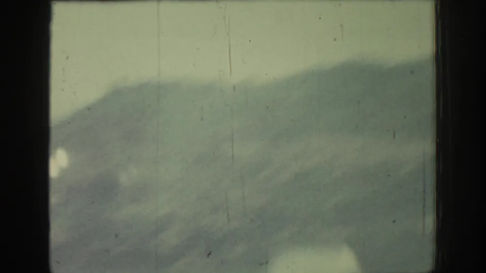 Soft 1962 8mm view from a car window toward distant hills in Rhodes, Greece, with visible film wear and haze.