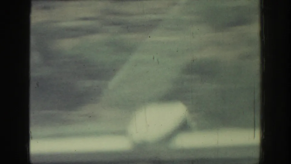 Moving-window view in Rhodes, Greece, with a dark vertical divider and pale blurred exterior shapes on soft 8mm film.