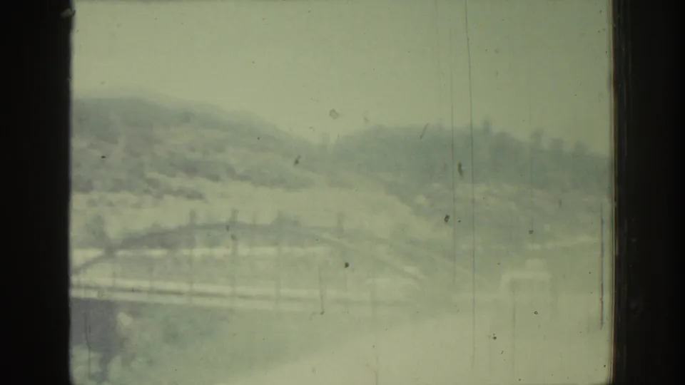 1962 Rhodes travel footage showing hazy hills and a bridge-like structure through a window, softened by motion and film grain.