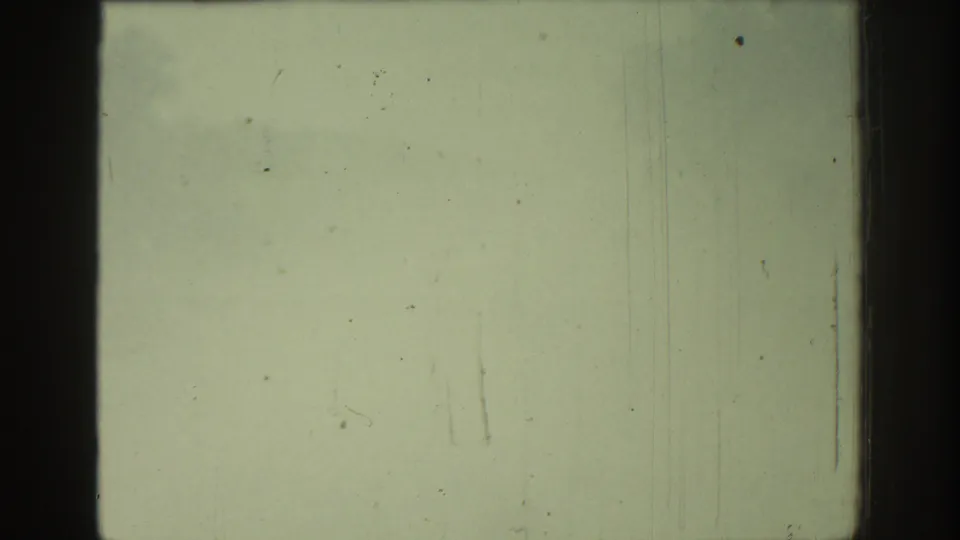 The frame fills with a pale passing surface, leaving mostly film texture, dust, scratches, and soft greenish exposure.