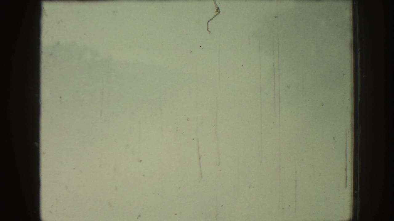 Overexposed 1962 Rhodes 8mm frame with greenish fading, vertical scratches, dust marks, and dark film-edge bands.