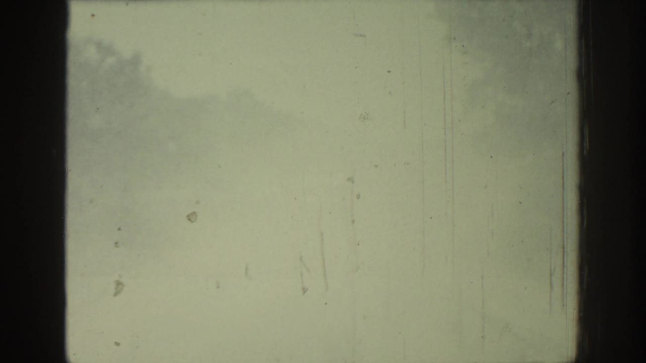 Faded Rhodes 1962 8mm frame showing washed exposure, dark film-frame bars, scattered dust, and faint cloudy density.